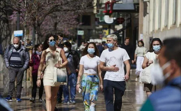People wearing masks walk down a street in Valencia.