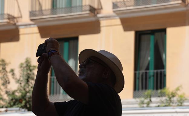 A tourist, protected from the sun with a hat, takes a photo in Malaga city centre./SALVADOR SALAS
