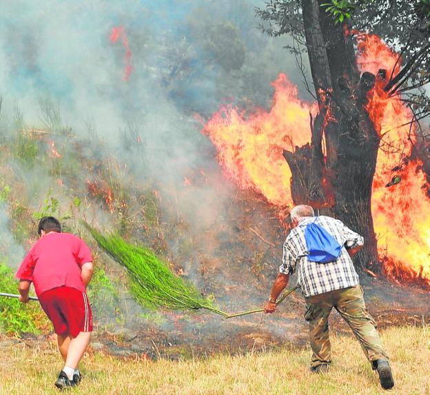 Two locals try to extinguish flames on land in Galicia this week. 